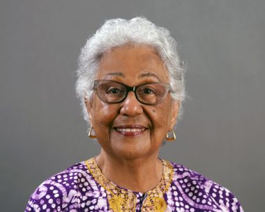 Daryl Cumber Dance, smiling, wears glasses and a purple, gold-trimmed top.