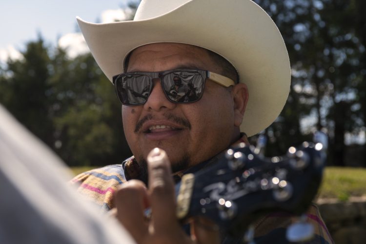 Man in cowboy hat and sunglasses plays guitar, reflecting sky