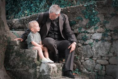 Father and son sitting on stone steps under tree, fatherhood