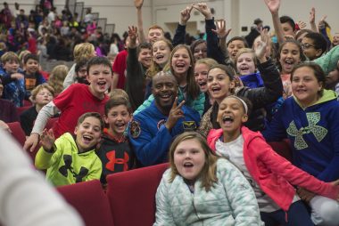 Diverse group of excited children and an astronaut in auditorium