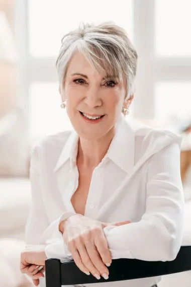 A smiling white woman with short gray hair in a white blouse.