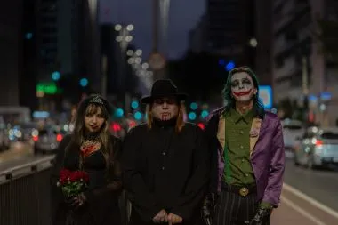 Three people in Halloween costumes: bride of Frankenstein, vampire, and Joker, at night.